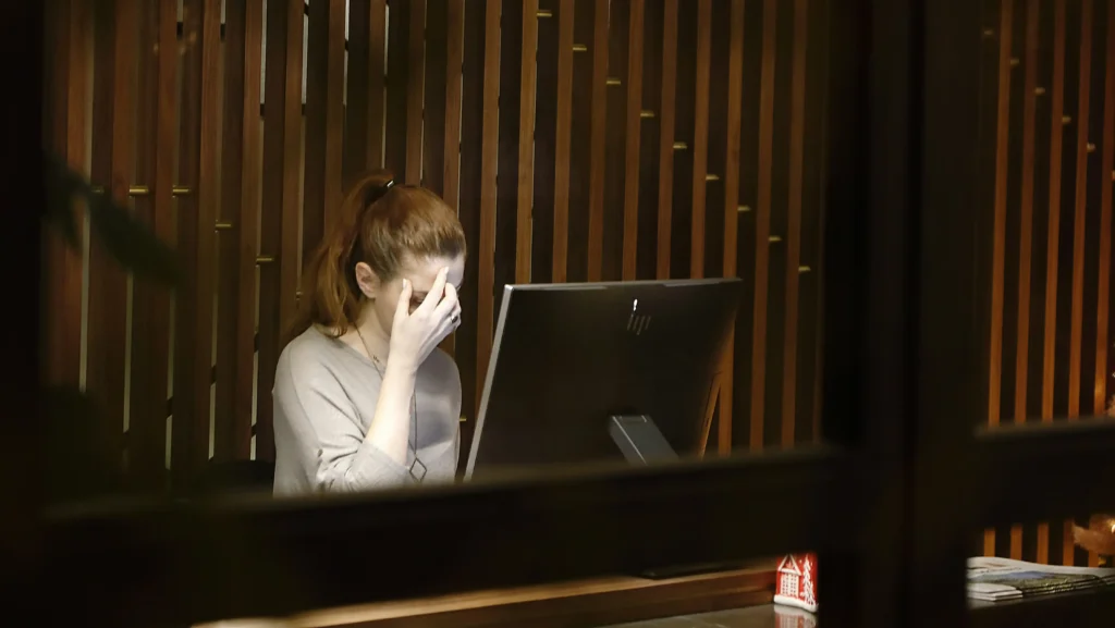 Mulher sentada à frente de um computador com as mãos na cabeça.
