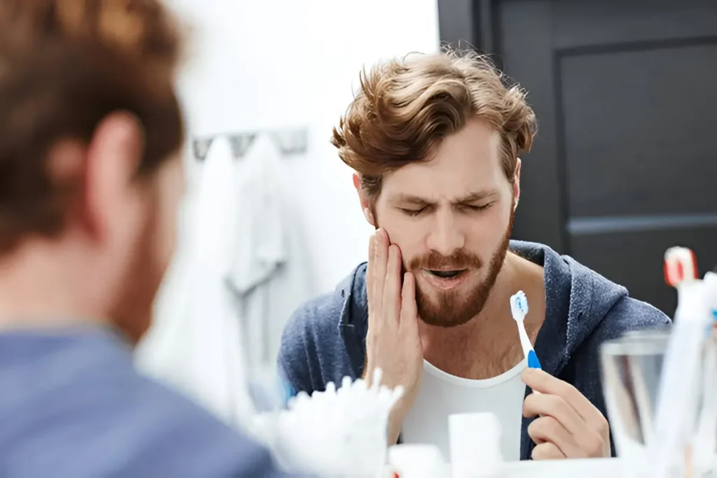 Homem com escova de dentes na mão a sentir sensibilidade nos dentes.