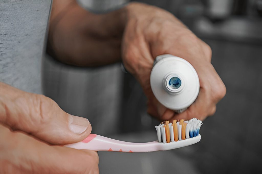 Pessoa a segurar uma escova de dentes a colocar pasta de dentes na mesma.